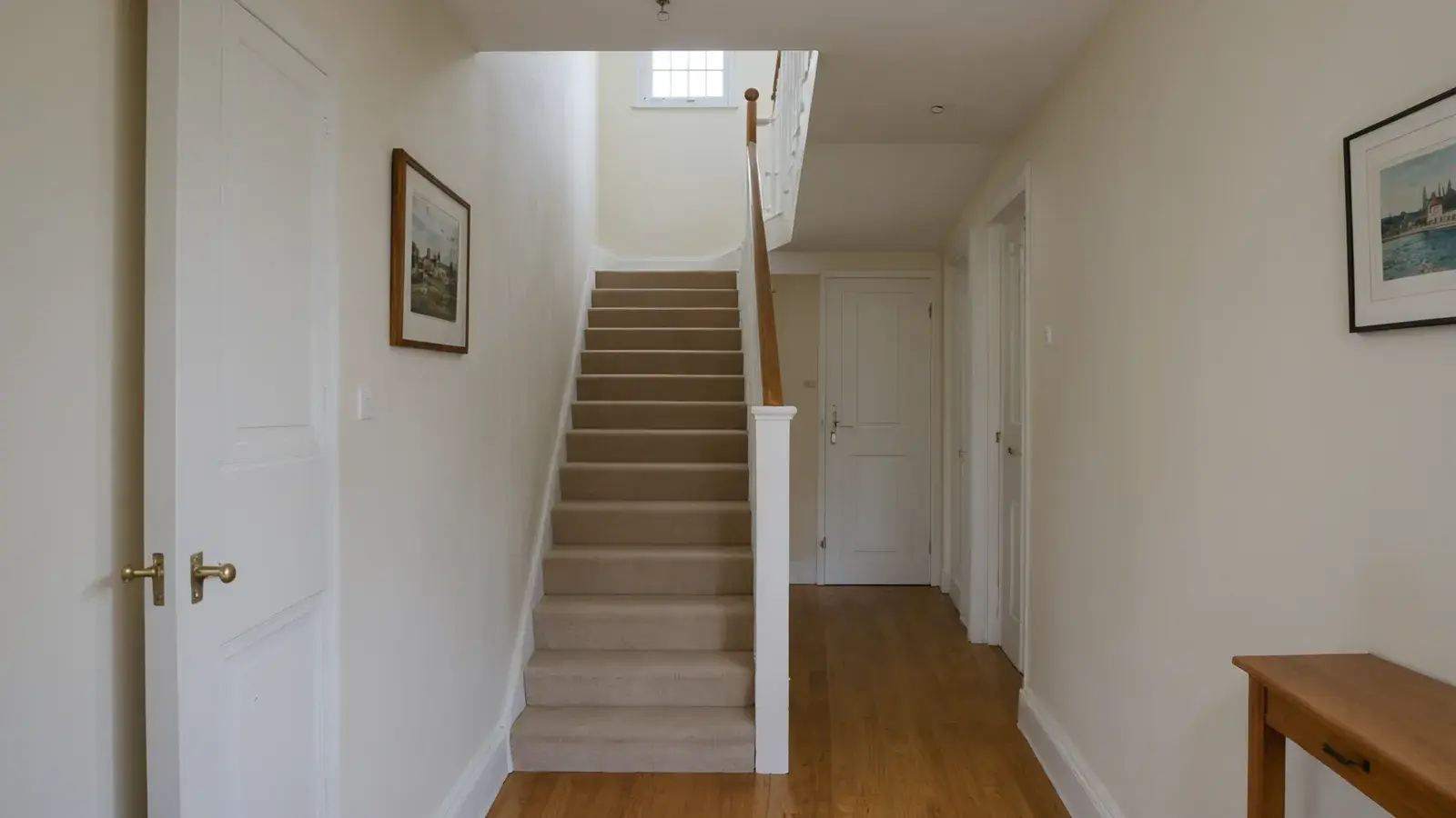 Couloir clair d'une maison : volée d'escalier droite moquettée montant vers un palier, main courante en bois, portes blanches